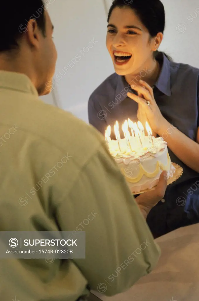 Mid adult man holding a birthday cake in front of a mid adult woman