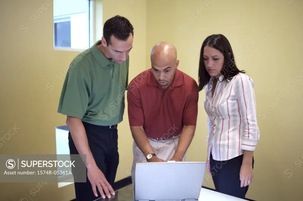 Two businessmen and a businesswoman looking at a laptop