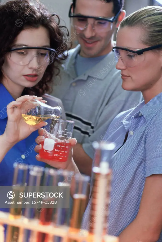 Two young women and a young man pouring liquid from a flask into a measuring beaker