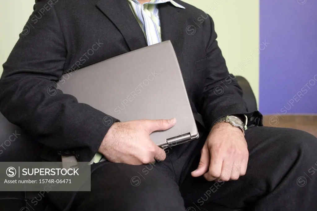 Mid section view of a businessman holding a laptop in an office