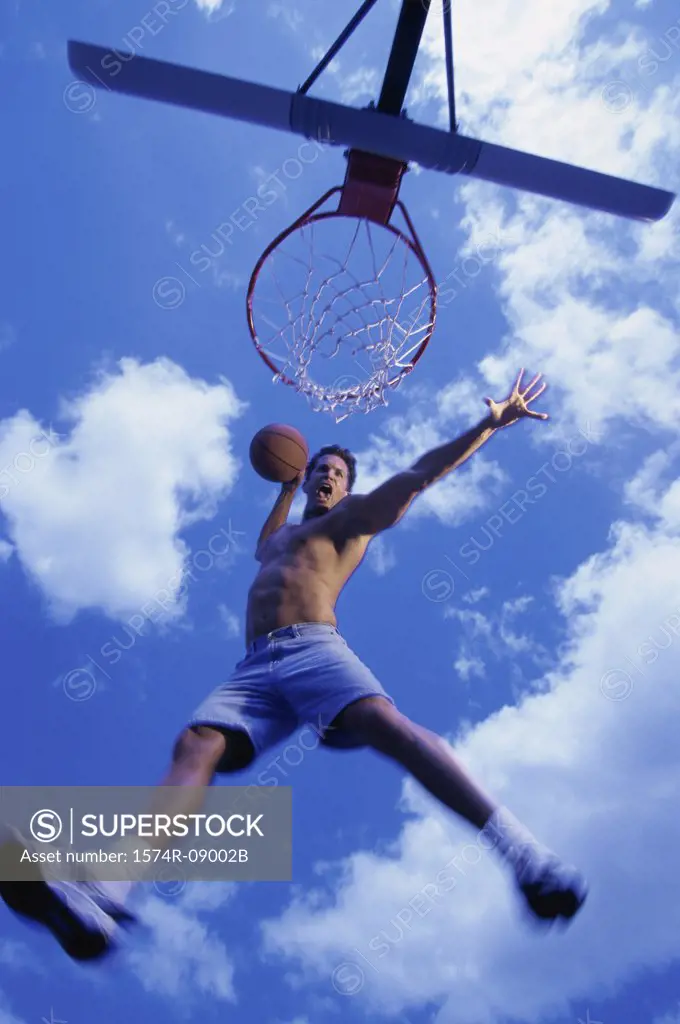 Low angle view of a young man slam dunking a basketball