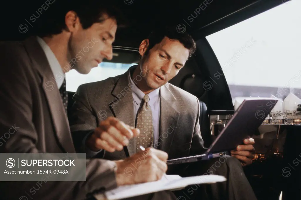 Two businessmen using a laptop in a car