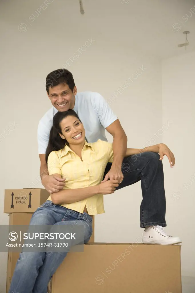 Young woman sitting on a cardboard box and smiling with a mature man standing behind her