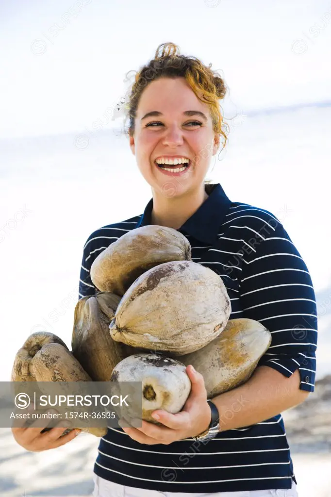 Woman holding coconuts and smiling on the beach, Tahaa, Tahiti, French Polynesia