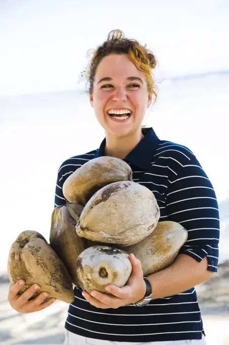 Woman holding coconuts and smiling on the beach, Tahaa, Tahiti, French Polynesia