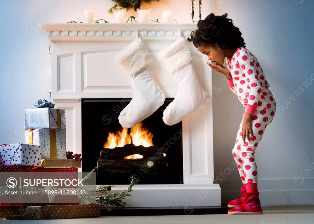 Surprised Black girl in pajamas looking down at Christmas gifts