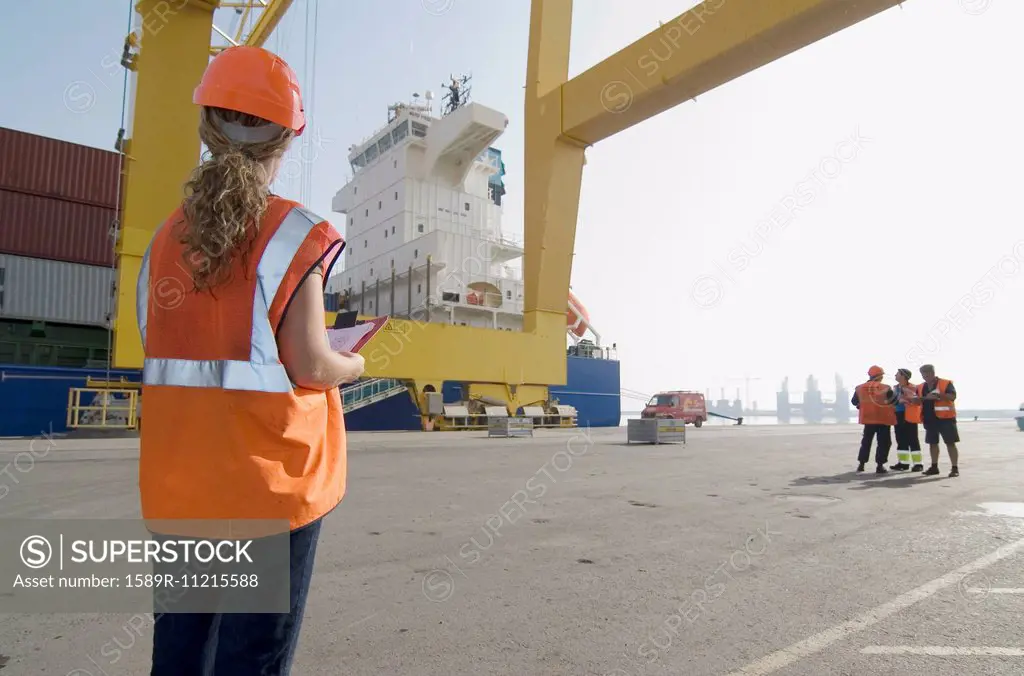 Woman wearing hard hat holding clipboard standing on dockside