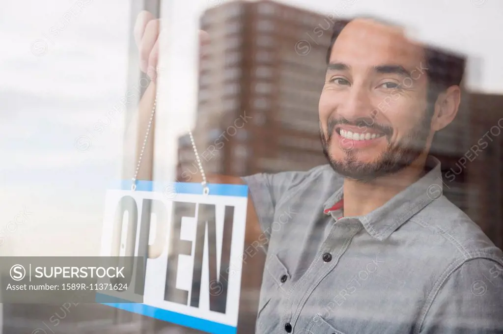 Mixed race man placing Open sign in shop window