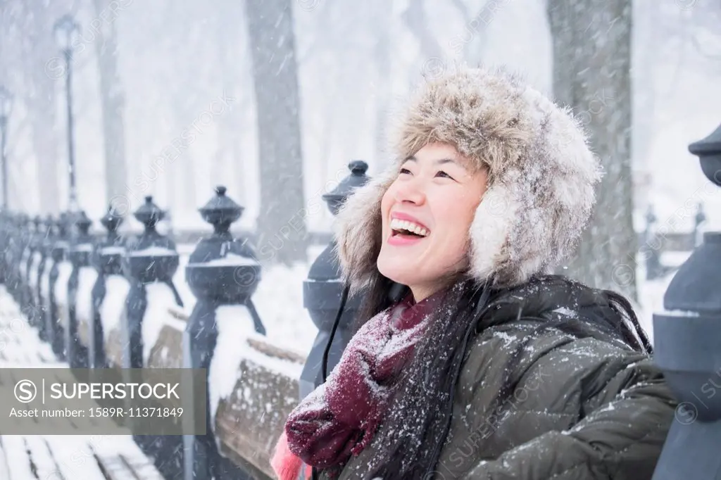 Asian woman sitting on park bench in snow