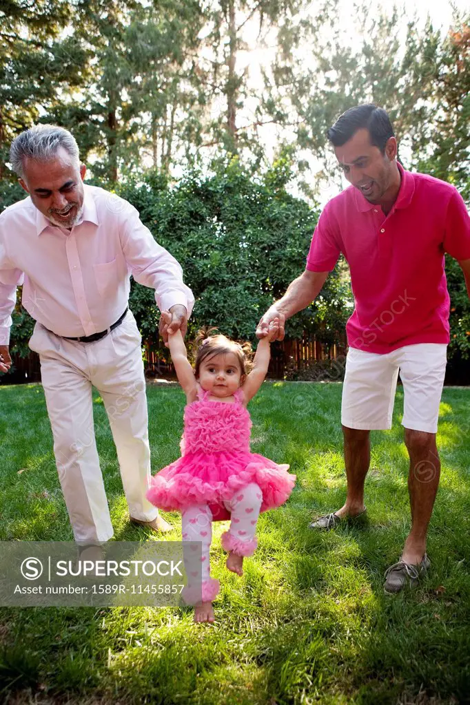 Father and grandfather helping daughter walk in backyard