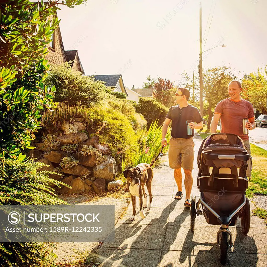 Caucasian gay couple walking dog and pushing stroller on sidewalk