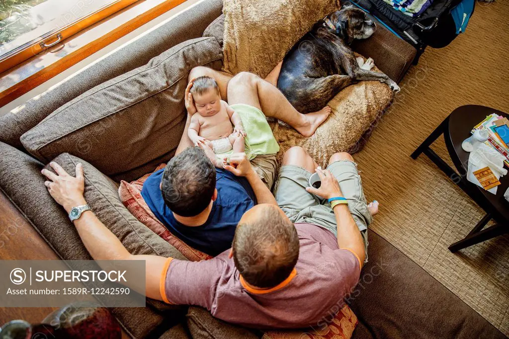 Caucasian gay couple holding sleeping baby boy on sofa