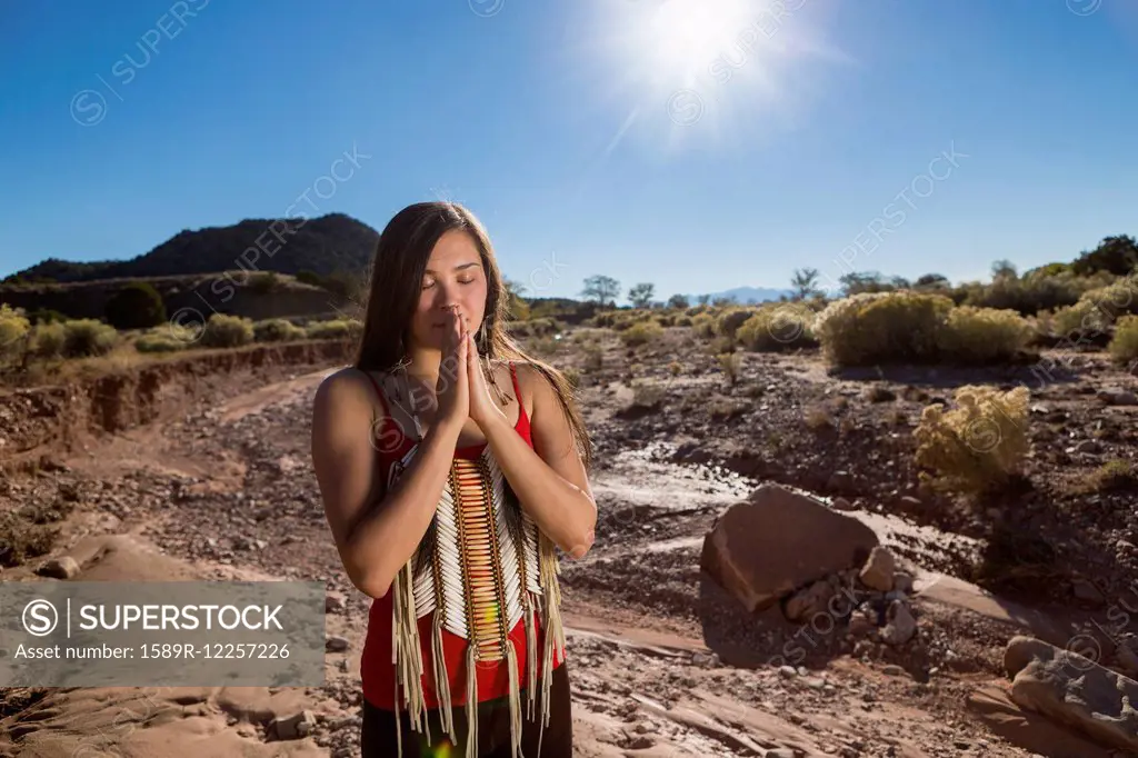 Mixed race woman praying in remote desert landscape