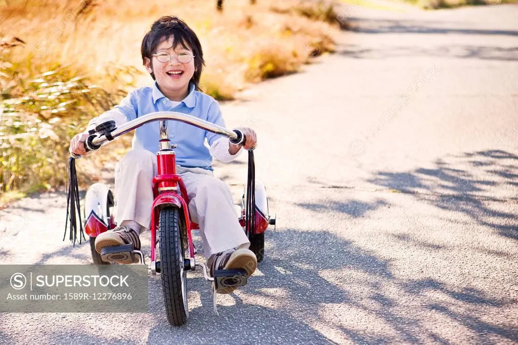 Chinese boy riding tricycle on sidewalk