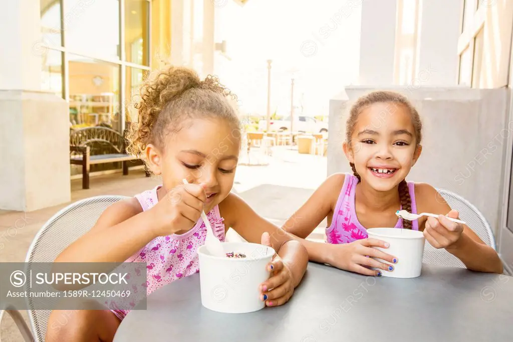 Mixed race sisters eating ice cream at outdoor cafe