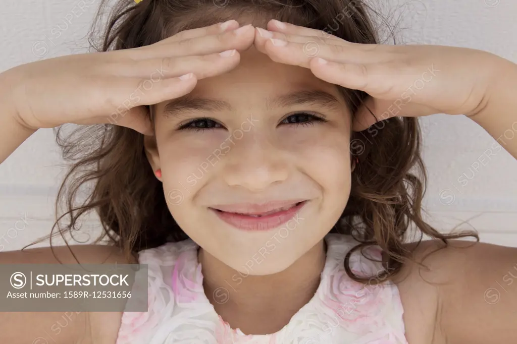 Smiling Hispanic girl shading eyes from the sun