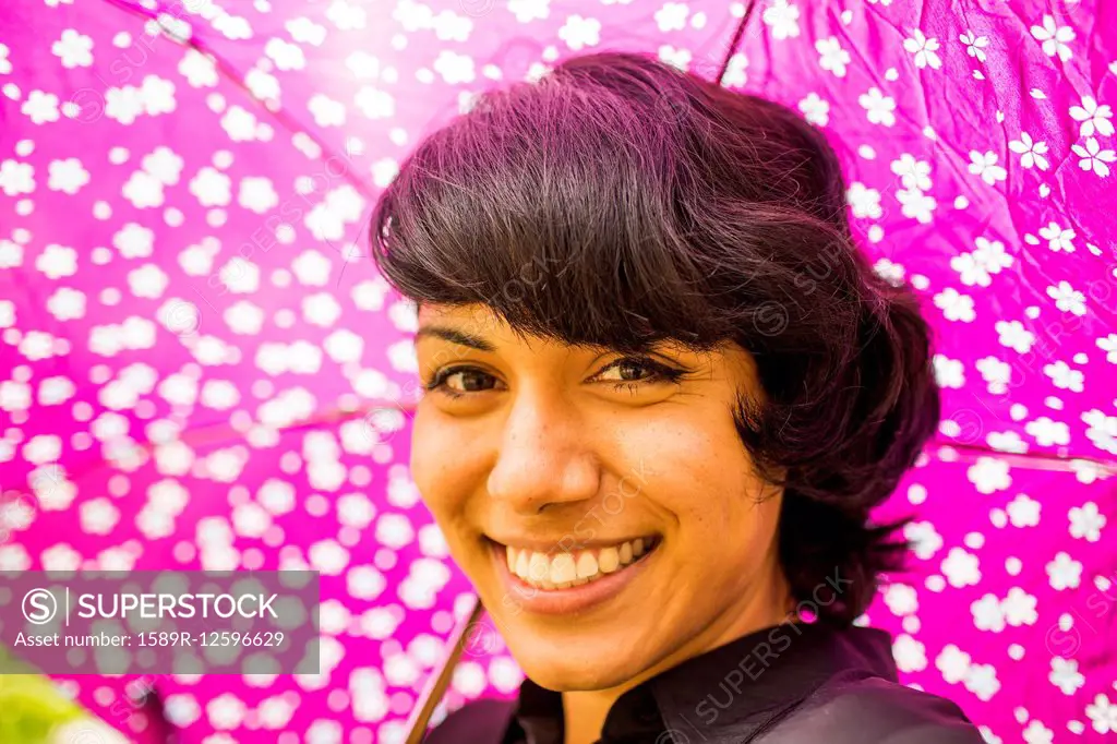 Smiling Hispanic woman holding pink umbrella