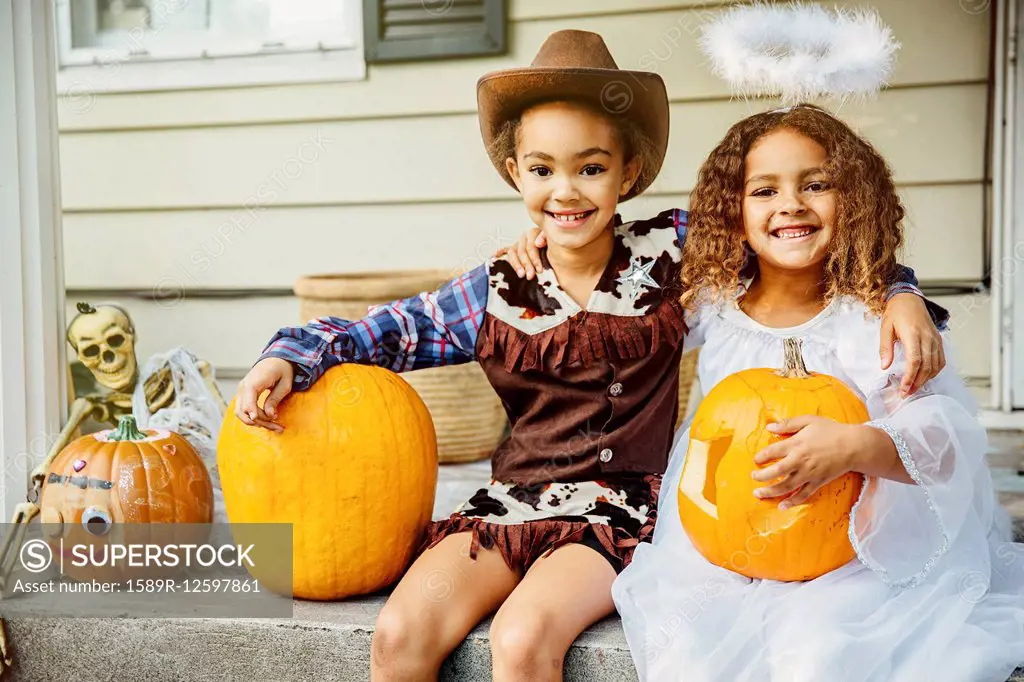 Sisters wearing Halloween costumes with jack-o-lanterns on porch