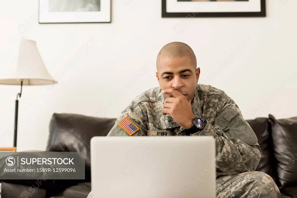 Mixed race soldier using laptop on living room sofa