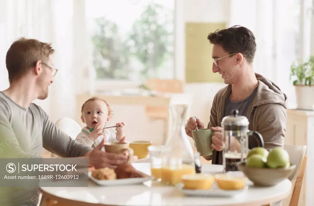 Caucasian gay fathers and baby eating breakfast