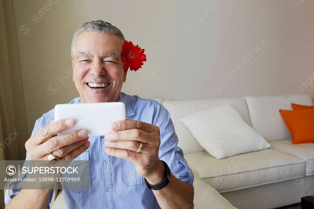 Older Black man taking selfie with flower behind his ear