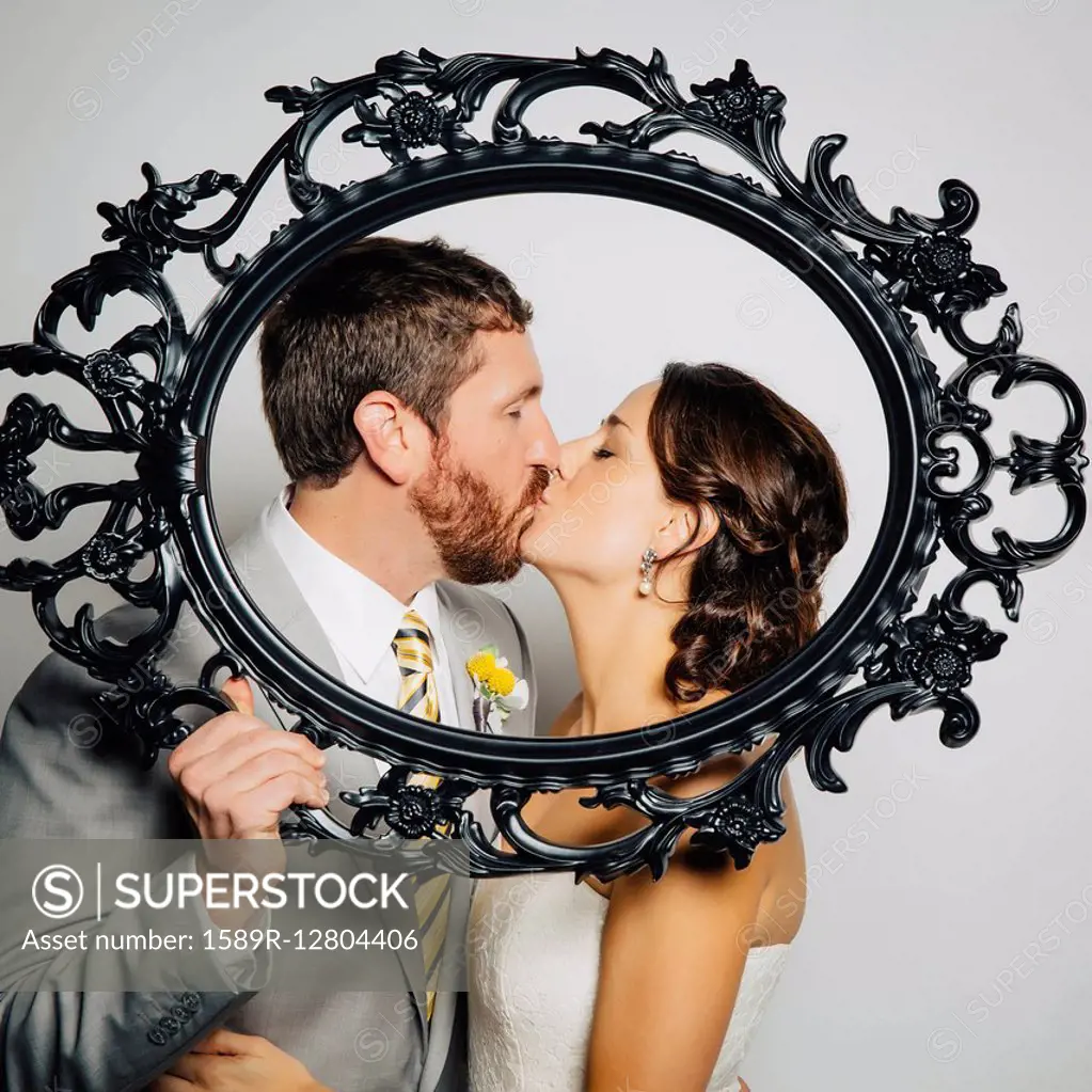 Caucasian bride and groom kissing behind empty frame