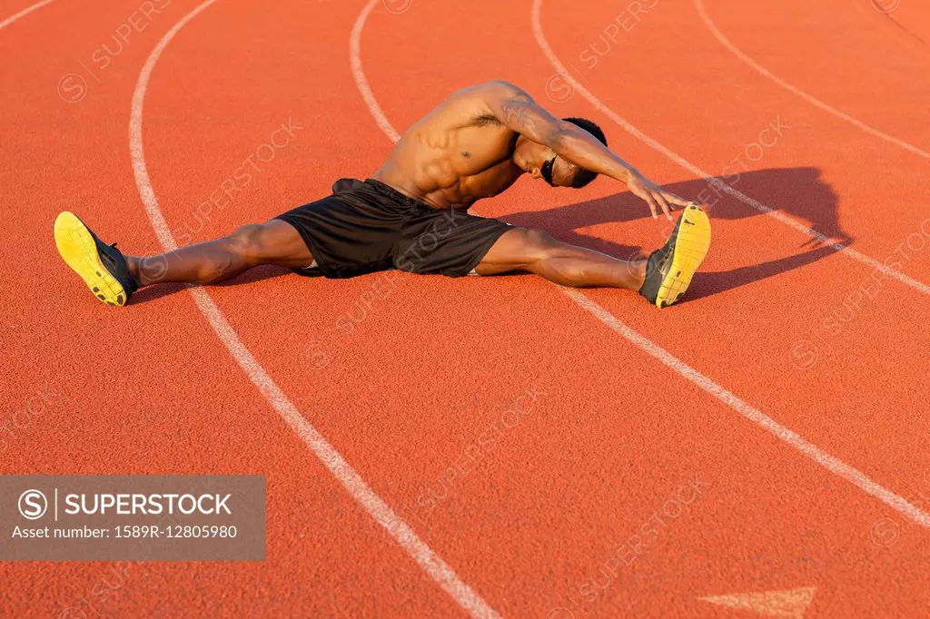 Black athlete stretching on track in sports field