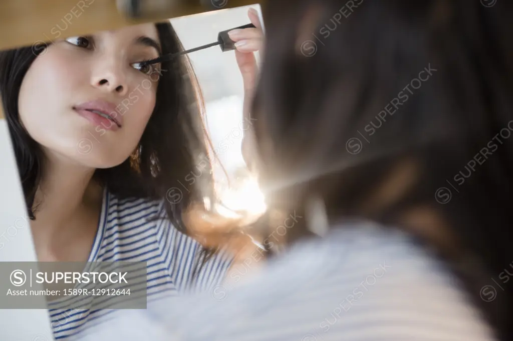 Hispanic woman applying mascara in mirror