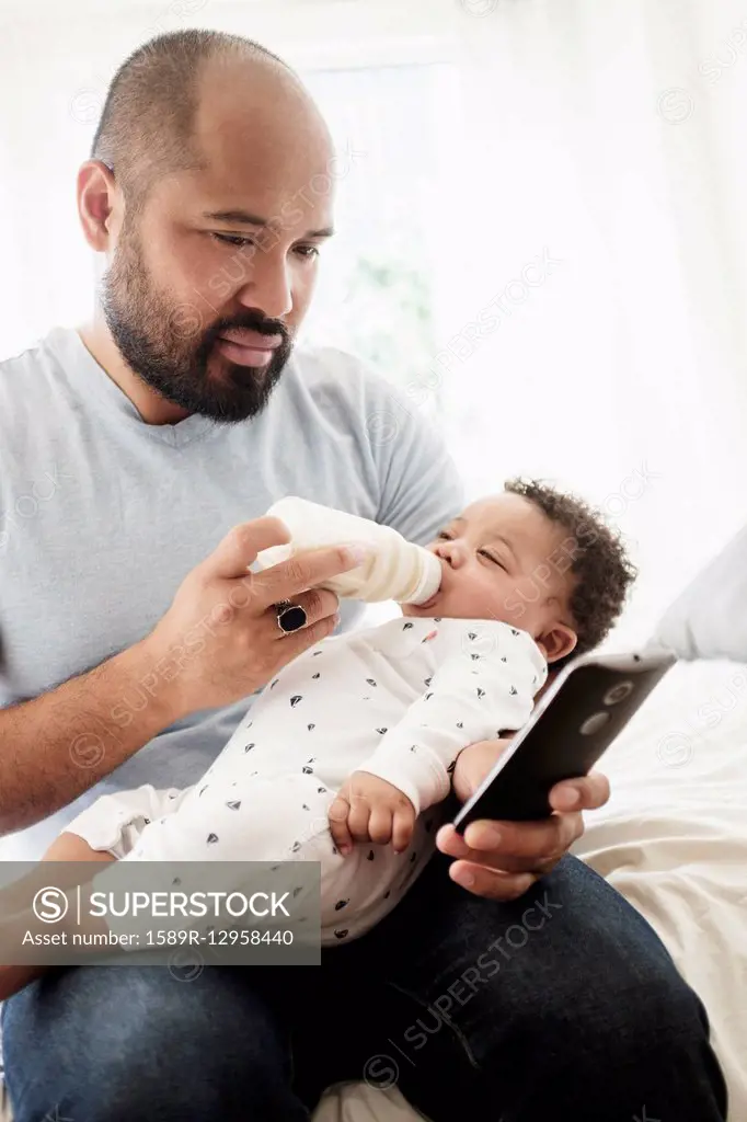 Father bottle feeding baby son and using cell phone