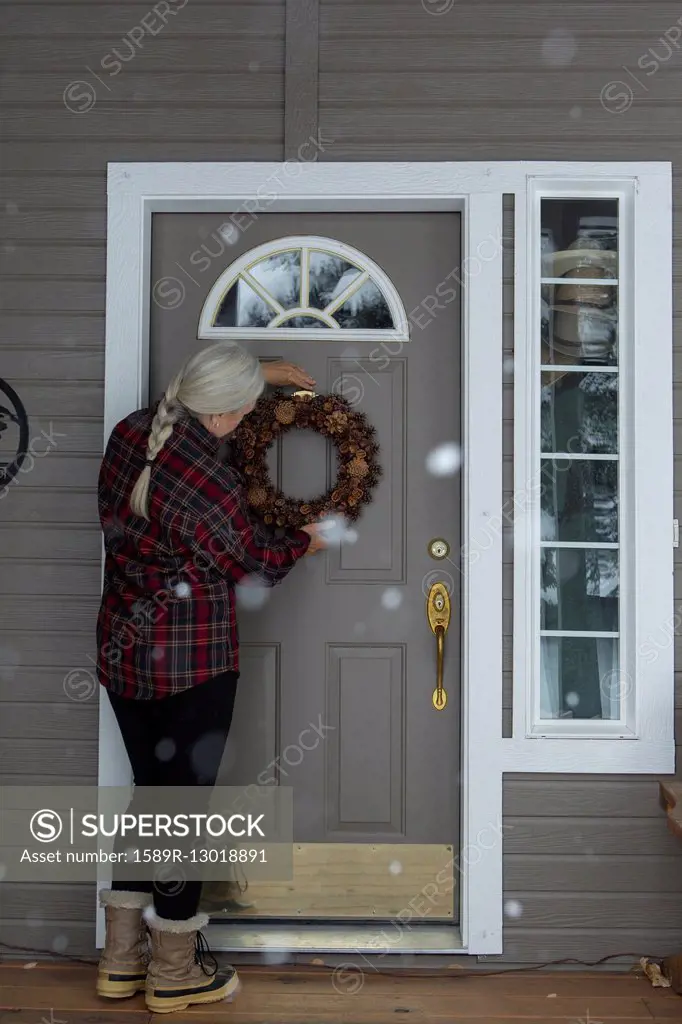 Older Caucasian woman hanging wreath on front door