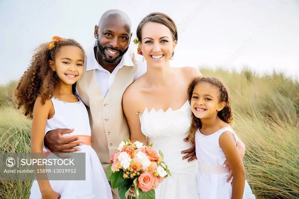 Newlywed couple and daughters smiling outdoors