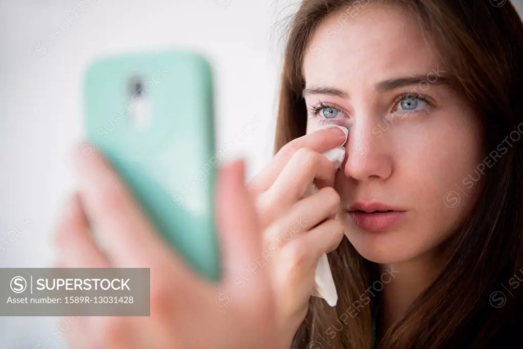 Native American woman with cell phone wiping away tears