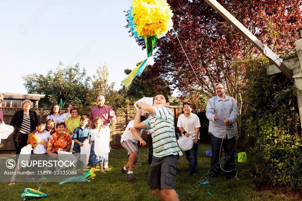 Hispanic family breaking pinata in backyard