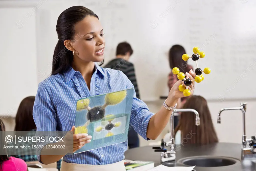 Black teacher holding digital tablet and chemistry model in classroom