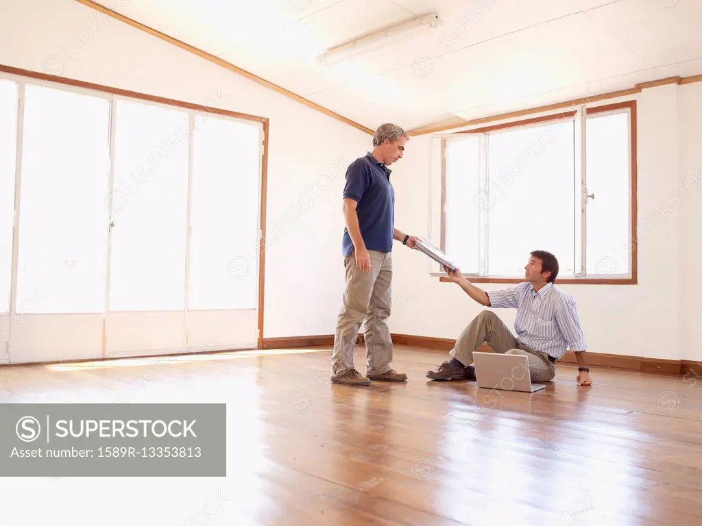 Hispanic businessman handing paperwork to co-worker in empty office