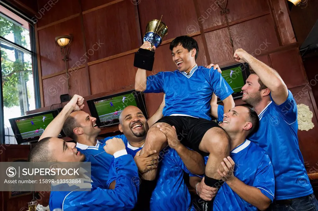 Cheering teammates lifting man holding trophy