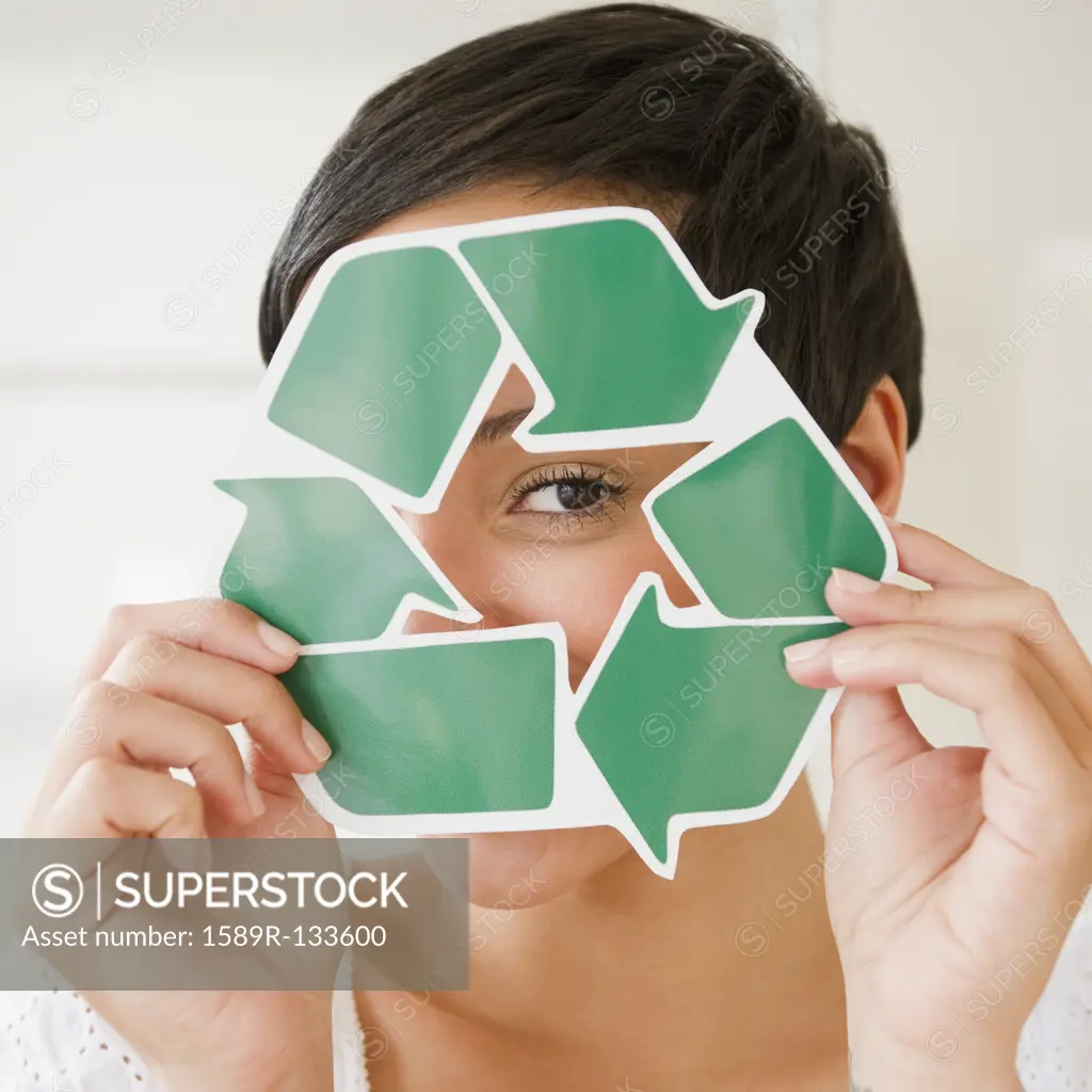 Mixed race woman holding recycling symbol in front of face
