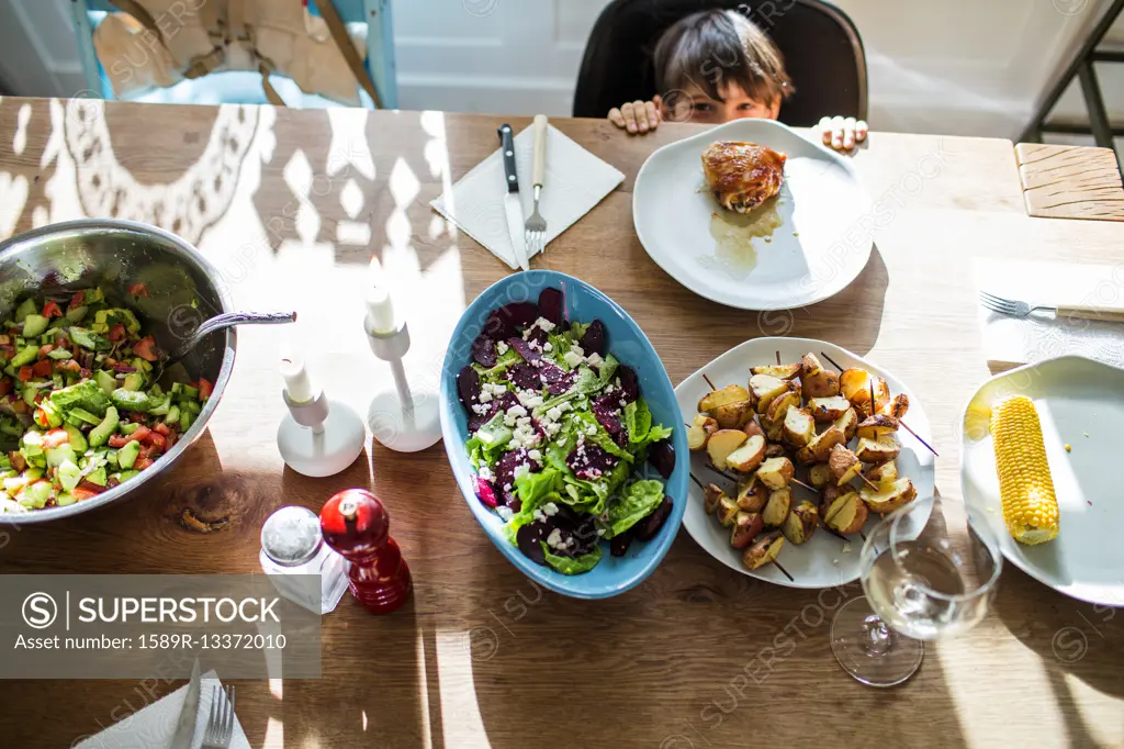 Mixed Race boy hiding behind table with food