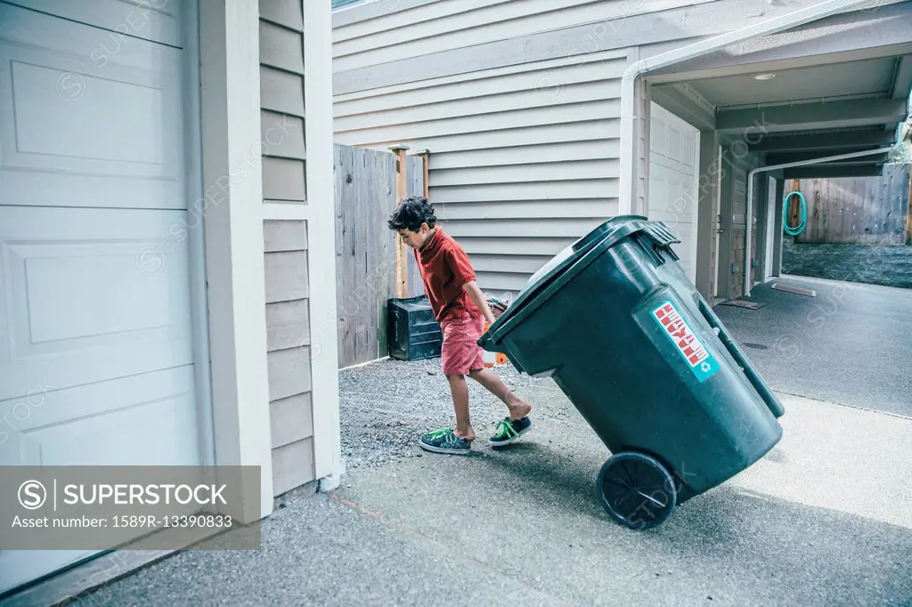 Mixed race boy pulling trash can in driveway