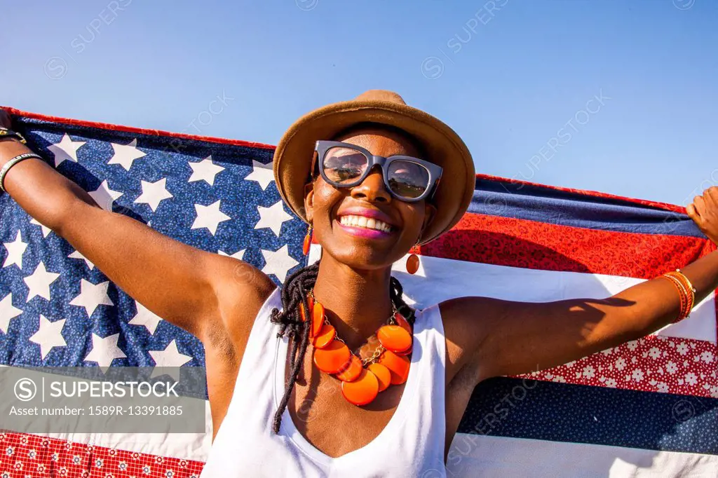 Black woman holding American flag under blue sky