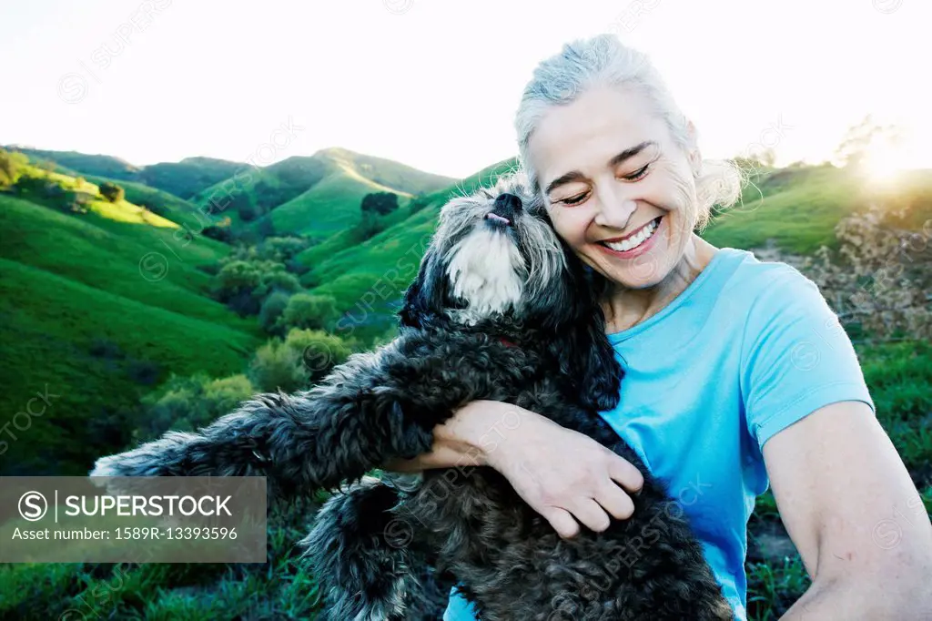 Older Caucasian woman hugging dog on rural hilltop