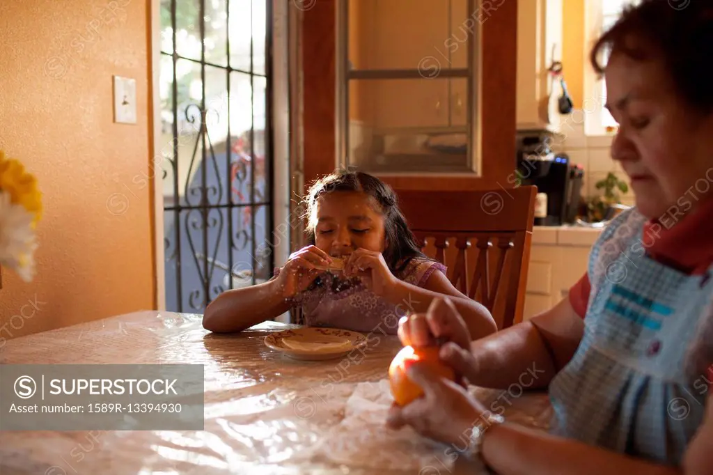 Hispanic grandmother and granddaughter eating in kitchen