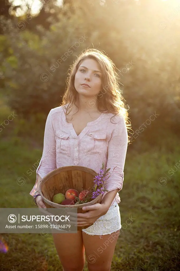 Woman carrying bucket of apples in field