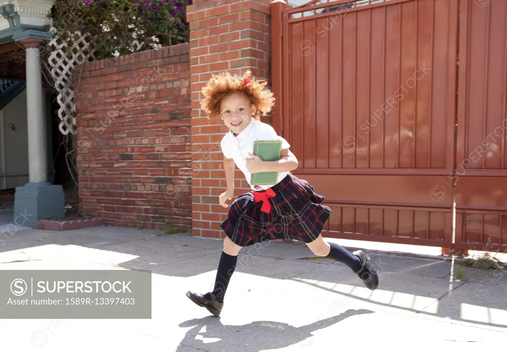 Smiling girl in school uniform running in driveway