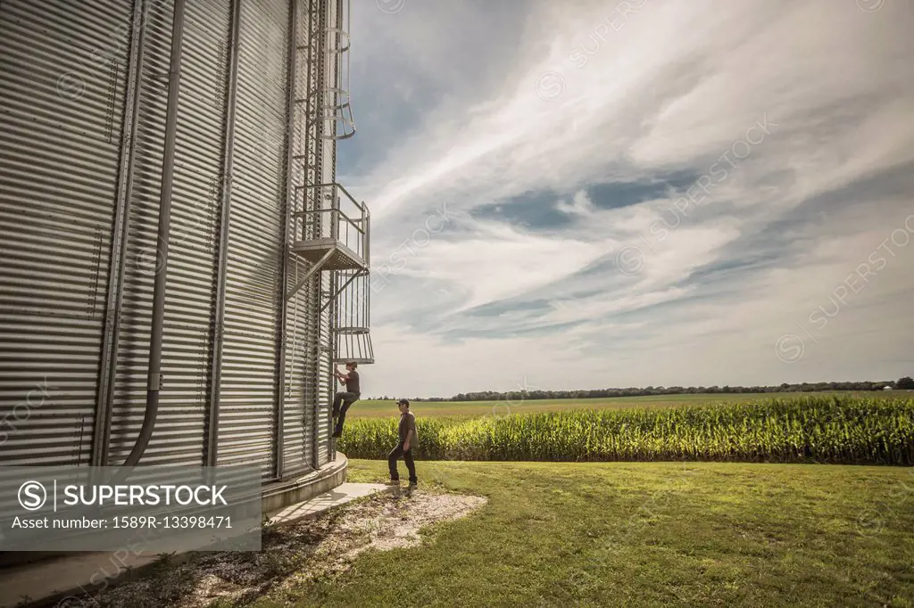 Caucasian farmer and son climbing grain silo