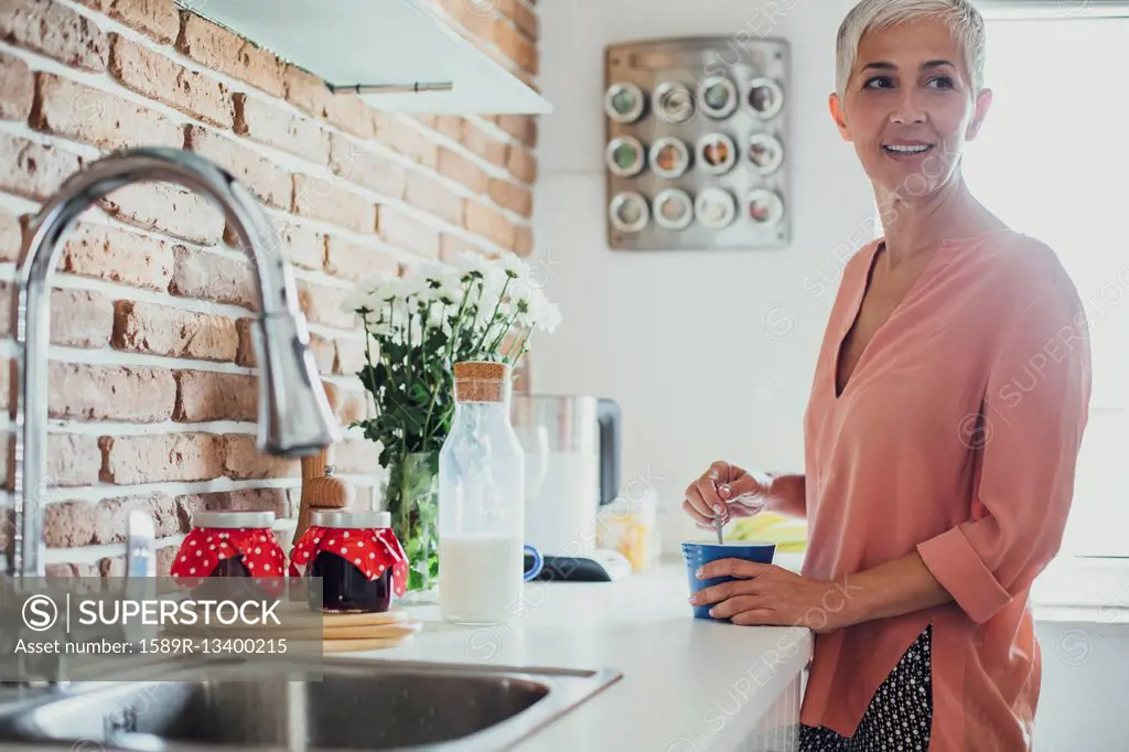 Older Caucasian woman stirring coffee in kitchen