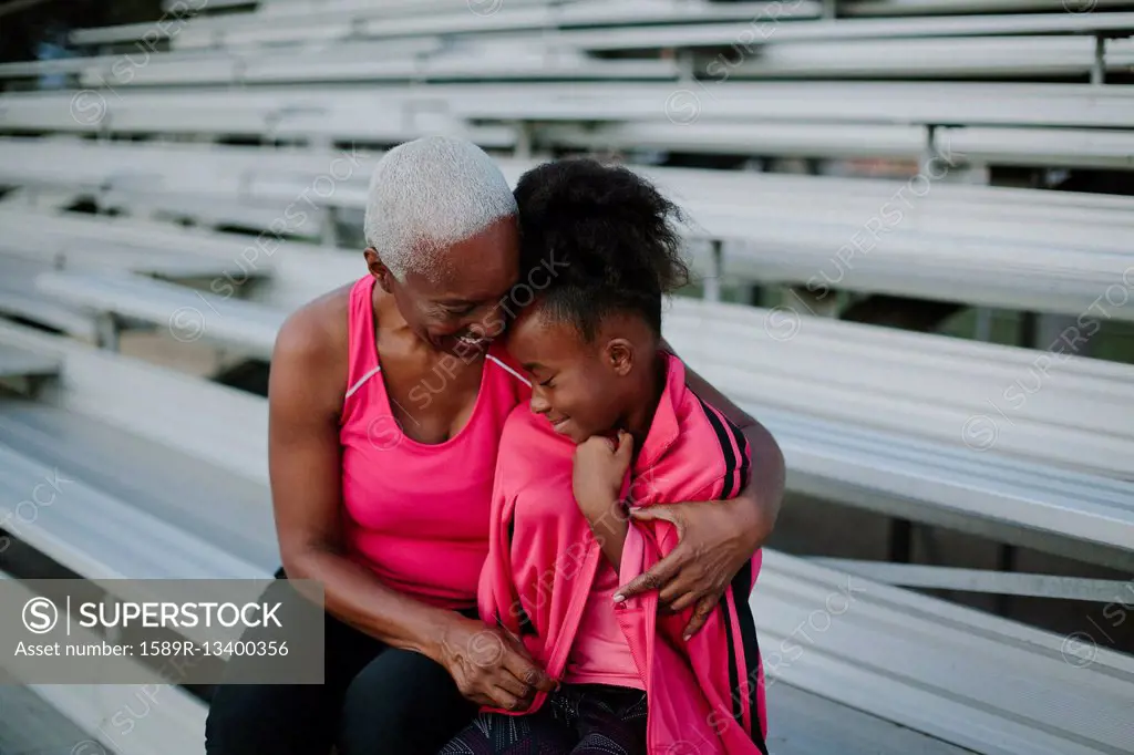 Grandmother wrapping sweater around granddaughter on bleachers