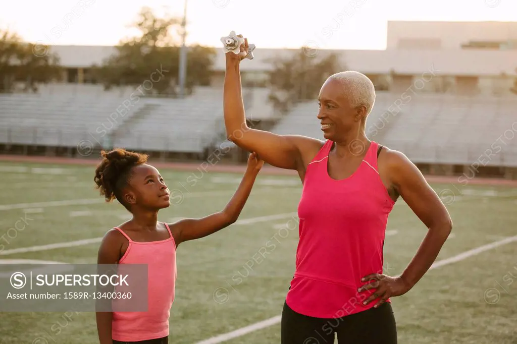 Girl squeezing biceps of grandmother on football field