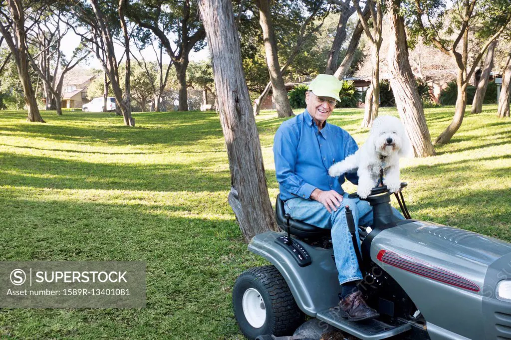Older Caucasian man on riding lawnmower with pet dog