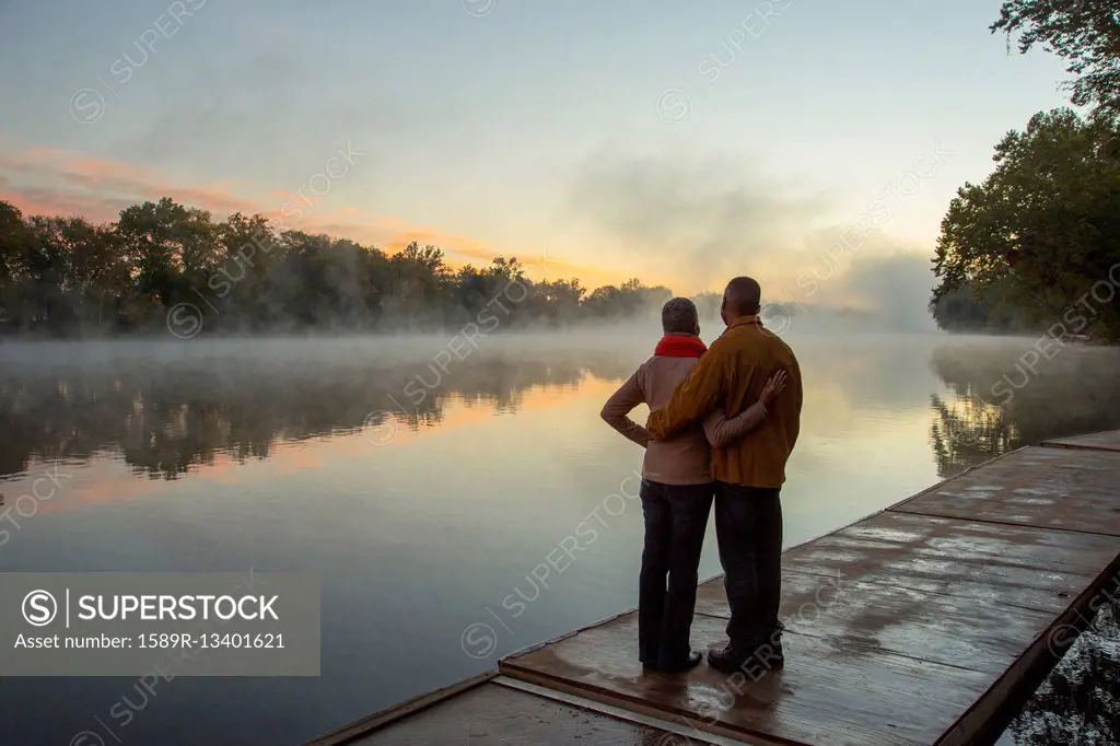 Older couple hugging at foggy river at sunrise